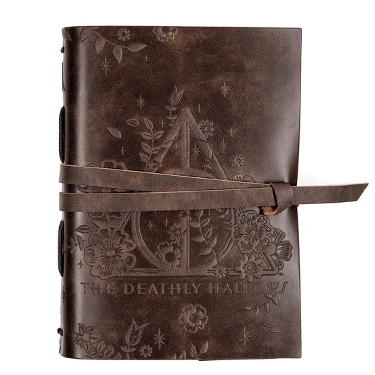 A brown vegan leather Harry Potter journal with blank lined pages and the Deathly Hallows symbol embossed on the cover. It has a wrap strap included for closure.